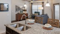 Elegant apartment interior featuring a modern granite kitchen island with stylish lighting, overlooking a cozy living room with contemporary decor.