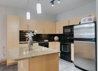 Kitchen with granite island, black tile backsplash, light wood cabinets, and stainless steel refrigerator