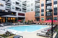 Jump In & Make Some Waves... Inviting outdoor pool area with loungers and umbrellas, surrounded by modern apartment buildings.