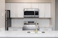 Modern Kitchen featuring marble style Quartz countertops and stainless steel appliances including microwave and pull down faucet in an Autumn Town Center apartment.