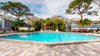 Pool with lounge chairs red umbrellas, exterior of apartment buildings, trees