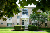 Charming apartment exterior with classic brick facade, lush greenery, and inviting entrance nestled under vibrant trees.