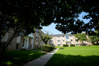 Charming apartment building nestled in lush green surroundings, featuring a peaceful pathway and well-maintained landscaping.