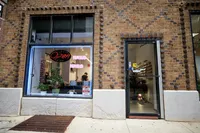 Charming nail salon storefront with neon 'Open' sign, vibrant plants, and inviting brick facade.