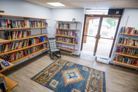 Cozy reading nook with bookshelves filled with colorful books, a comfy rocking chair, and an inviting patterned area rug next to large glass doors.