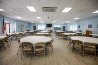 Spacious event room with round tables, elegant lighting, and warm wooden flooring, ideal for gatherings and meetings.