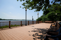 Scenic waterfront deck with inviting benches, surrounded by lush greenery and panoramic river views.