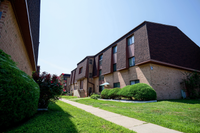 Charming brick apartment complex with lush greenery and a welcoming path, perfect for tranquil living.