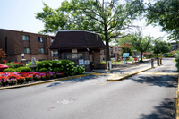 Charming gated community entrance with colorful flower beds and brick architecture, surrounded by lush greenery and mature trees.