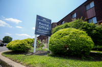 Welcoming rental office sign amidst lush greenery at Delaire Landing Apartments, basking in bright sunlight.