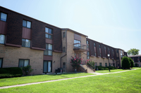 Charming brick apartment complex with manicured lawns and inviting entrance, basking in sunlight.