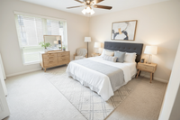 Elegant bedroom featuring a plush bed with a gray headboard, stylish wooden furniture, and abundant natural light through large windows.