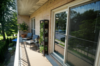 Charming apartment balcony with cozy seating, lush greenery, and serene views of a tree-lined street.