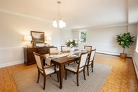 Bright and elegant dining room featuring a classic wooden table set for six, adorned with beautiful flowers, warm lighting, and a cozy ambiance.