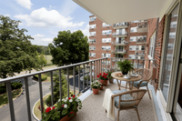 Charming apartment balcony with cozy outdoor seating, vibrant flowers, and scenic views of lush trees and neighboring buildings.