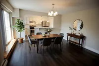 Elegant dining area with modern dark wood flooring, featuring a stylish table with six chairs, a vibrant plant by the window, and a connected upscale kitchen.