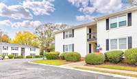 Charming apartment complex surrounded by lush greenery and bright blue sky, featuring well-maintained landscaping and inviting exterior design.