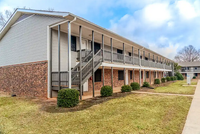 Charming two-story apartment complex with brick facade and inviting outdoor spaces, set against a clear blue sky.