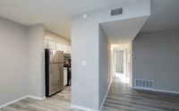 Modern apartment interior featuring a sleek stainless steel kitchen next to a bright hallway with stylish gray flooring.