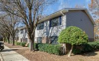 Charming brick and siding apartment building nestled among mature trees on a sunny day, offering serene suburban living.