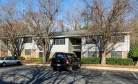Charming apartment complex with cozy two-story units surrounded by lush greenery and convenient parking.