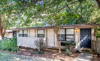 Charming single-story home with a modern black door, surrounded by lush greenery and inviting pathway.