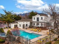 Inviting apartment complex with a sparkling outdoor pool, surrounded by lush landscaping and vibrant yellow lounge chairs, set against a backdrop of beautiful mountains.
