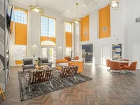 Luxurious living room with high ceilings, vibrant orange accents, modern furnishings, abundant natural light, and a stylish open-plan design.