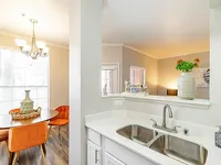 Elegant open-concept apartment kitchen with dual sinks, modern lighting, and cozy dining area adorned with vibrant orange chairs and decorative accents.