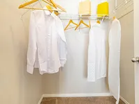 Bright walk-in closet with neatly hung clothes on wooden hangers, featuring ample storage space and modern design.