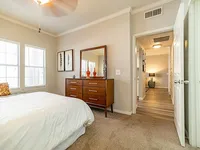 Bright and inviting bedroom with plush carpeting, elegant dresser, and hallway access to a modern apartment.