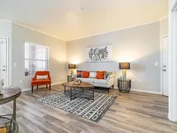 Bright and inviting living room with modern decor, featuring a cozy white sofa, vibrant orange accents, stylish coffee table, and elegant lighting on beautiful wooden flooring.