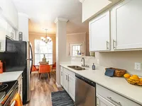 Bright and modern kitchen with sleek white cabinets, elegant countertops, and a cozy dining area with stylish orange chairs, illuminated by a chic chandelier.