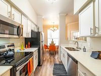 Bright and modern kitchen with stainless steel appliances, elegant white cabinetry, and an inviting dining area with chic orange chairs.