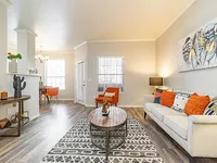 Inviting living room with modern decor, featuring a cozy sofa with colorful cushions, a stylish round coffee table, and elegant hardwood flooring. Bright natural light enhances the welcoming atmosphere.