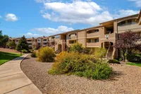 Charming apartment complex with appealing stone landscaping, vibrant greenery, and a tranquil walkway under a bright blue sky.