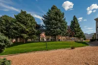 Breathtaking apartment view showcasing lush green lawns, majestic pine trees, and a serene pathway under a clear blue sky.