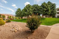 Serene apartment landscape showcasing lush green lawns, meticulously arranged gravel, and majestic trees with a backdrop of mountain views.