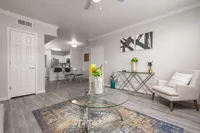 Bright and modern living area with elegant decor and open-concept design, featuring a stylish glass coffee table, cozy seating, and sleek kitchen in the background.