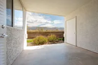 Charming outdoor patio area with a partial mountain view, framed by blooming shrubs and a textured wall, creating a serene and inviting atmosphere.