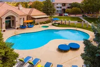 Elegant apartment community featuring a sparkling outdoor pool with stylish lounge areas and vibrant umbrellas, surrounded by lush greenery.
