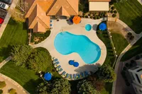 Aerial view of a luxurious apartment complex featuring a stunning outdoor swimming pool, surrounded by lush green landscaping and elegant lounge chairs for relaxation.