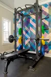 Contemporary home gym with vibrant geometric wall design, featuring a professional weightlifting setup and ample natural light.