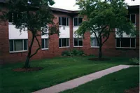 Charming apartment exterior with lush green lawn and mature trees, perfect for a serene living environment.