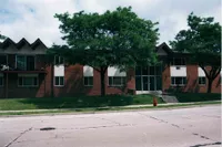 Charming suburban brick apartment building with lush green trees and a manicured lawn.