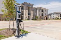 Modern apartment complex with elegant stone facades and outdoor EV charging station, surrounded by well-maintained landscaping and spacious parking lot.