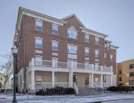 Charming brick apartment building with classic architecture, featuring large windows and a welcoming front porch.