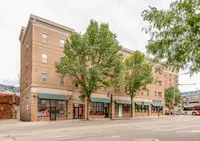 Charming brick apartment building with street-level shops, nestled amongst lush trees.