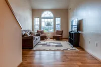 Bright living room with large arched window, comfortable seating, and modern TV setup, offering a welcoming ambiance.