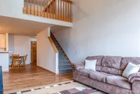 Inviting duplex living space with plush seating, warm wood flooring, and an open staircase leading to a cozy loft area.